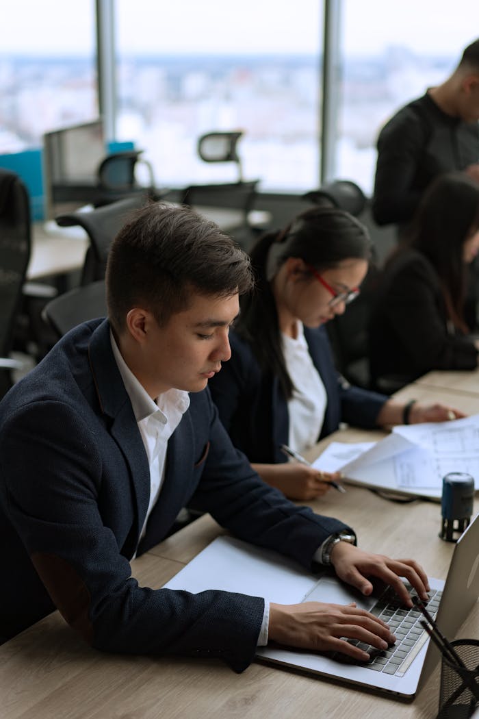 Business professionals working on laptops in an office with a city view, focused and busy.
